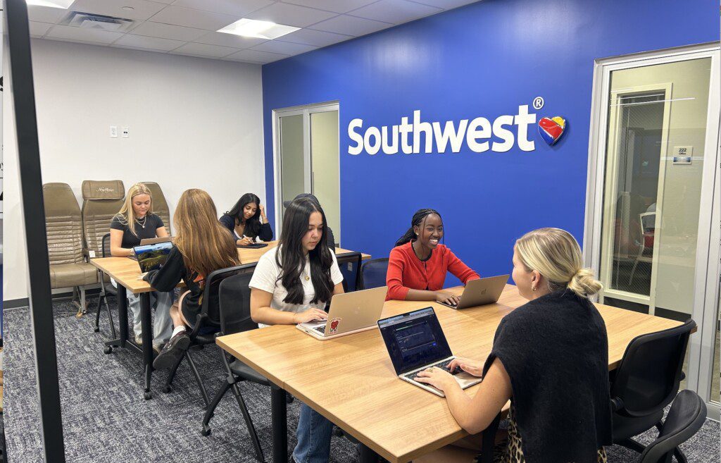 Students at the tables with their laptops studying. Southwest Airlines logo on the wall.