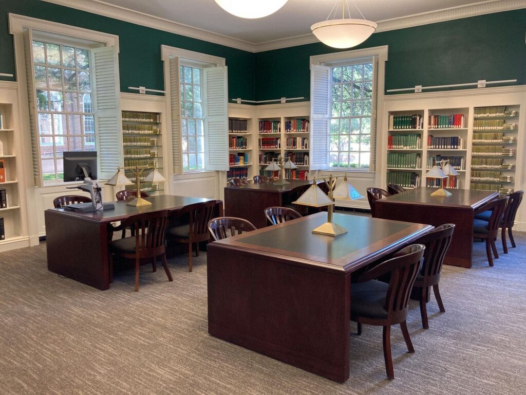 Four tables with lamps and chairs, along with a library of books behind.