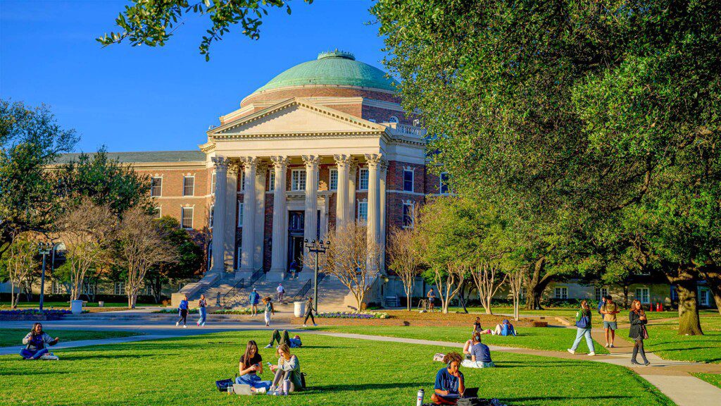 Over a dozen students sitting and doing homework on the Dallas Hall Lawn on a sunny day. 