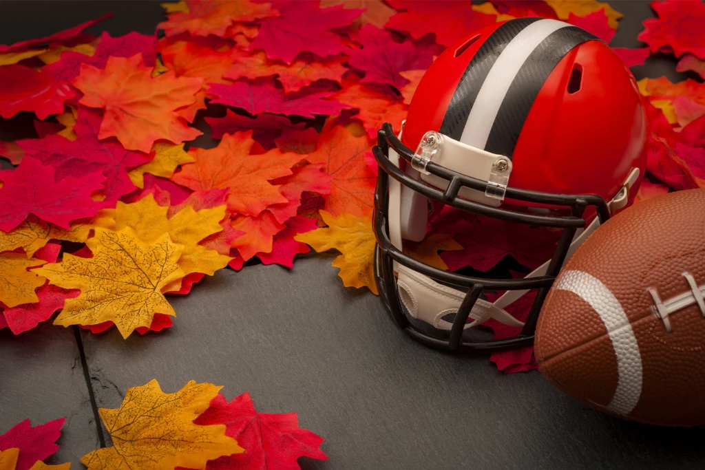 A football and a helmet sitting on a bed of fall leaves