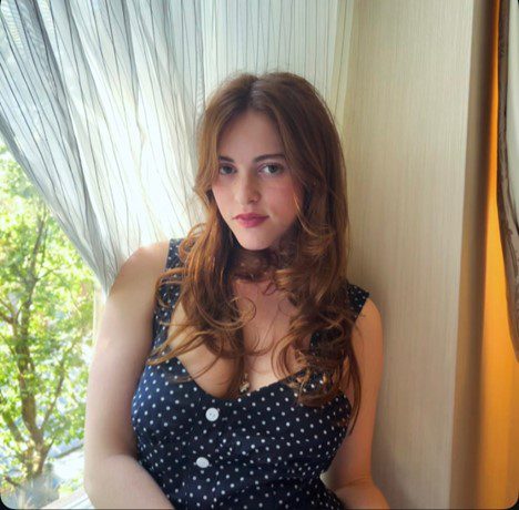 Julia Preston wearing a blue dress with white polka dots, sitting next to a window