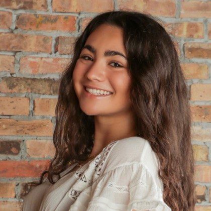Picture of Yasmine Boueri smiling in front of brick wall.