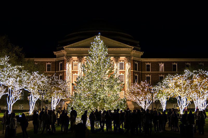 Dallas Hall illuminated and surrounded by trees. People are shown watching.