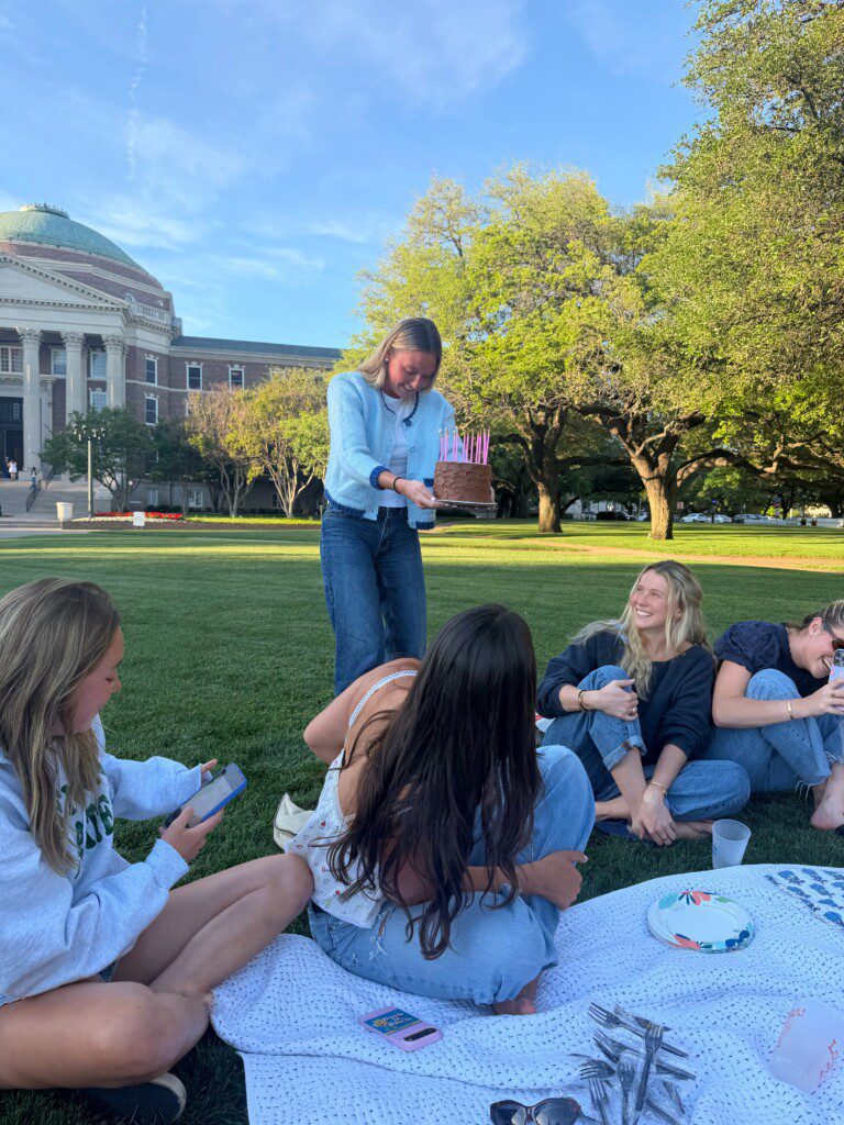 Shows a Picnic on Dallas Lawn with friends sitting on a blanlet.